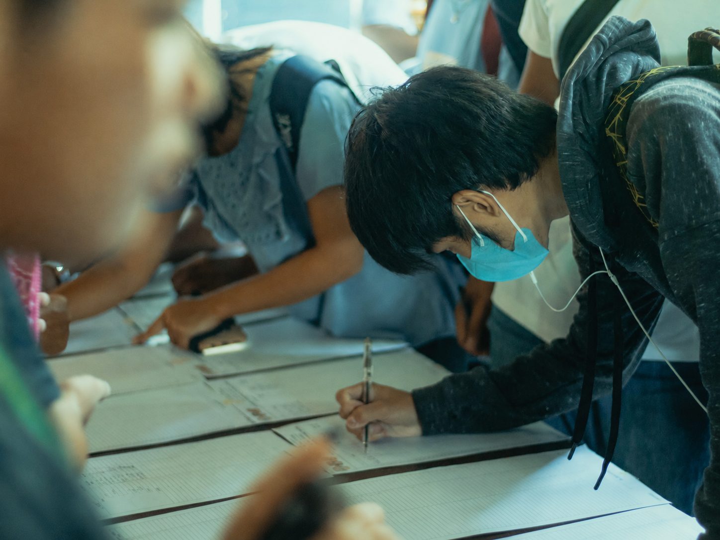 A student bent over a table filling up a paper form by hand